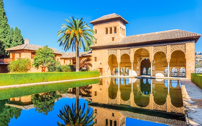 Alhambra palace reflecting in pool on a sunny day in Granada, Spain.