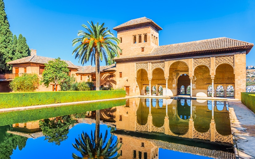 Alhambra palace reflecting in pool on a sunny day in Granada, Spain.