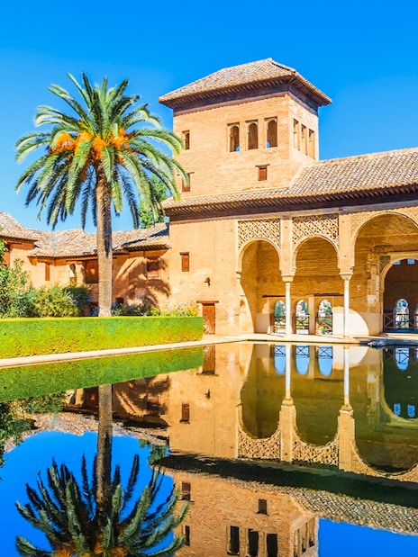 Alhambra palace reflecting in pool on a sunny day in Granada, Spain.