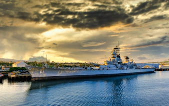 Battleship docked at Pearl Harbor, Hawaii, under dramatic sky, part of self-guided tour experience.