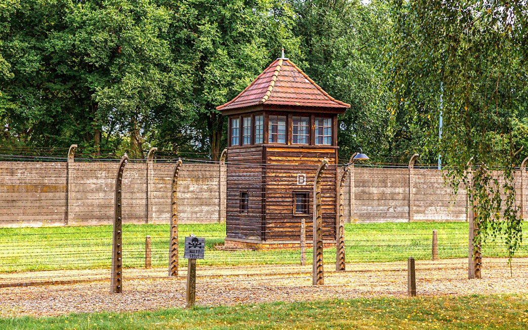 Watchtower at Auschwitz-Birkenau Camp with barbed wire fence and trees in the background.
