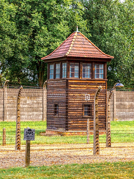 Watchtower at Auschwitz-Birkenau Camp with barbed wire fence and trees in the background.