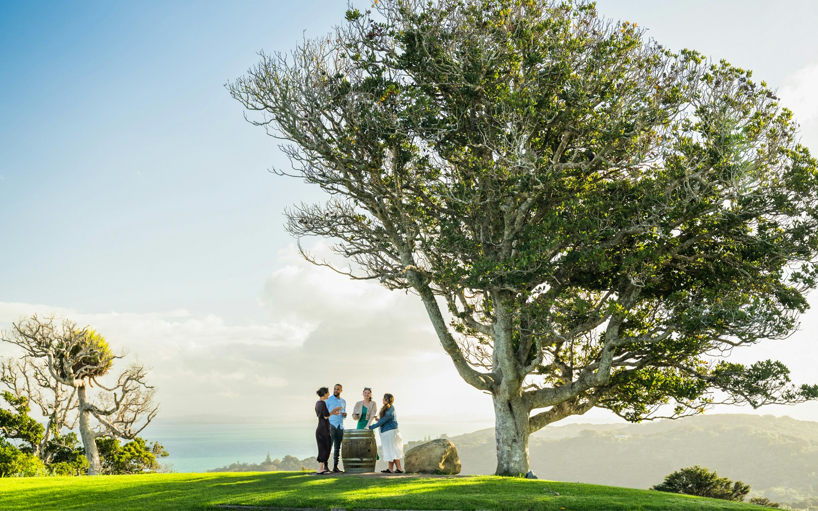 Group enjoying wine at Batch Winery, Waiheke, with views of Hauraki Gulf Islands.