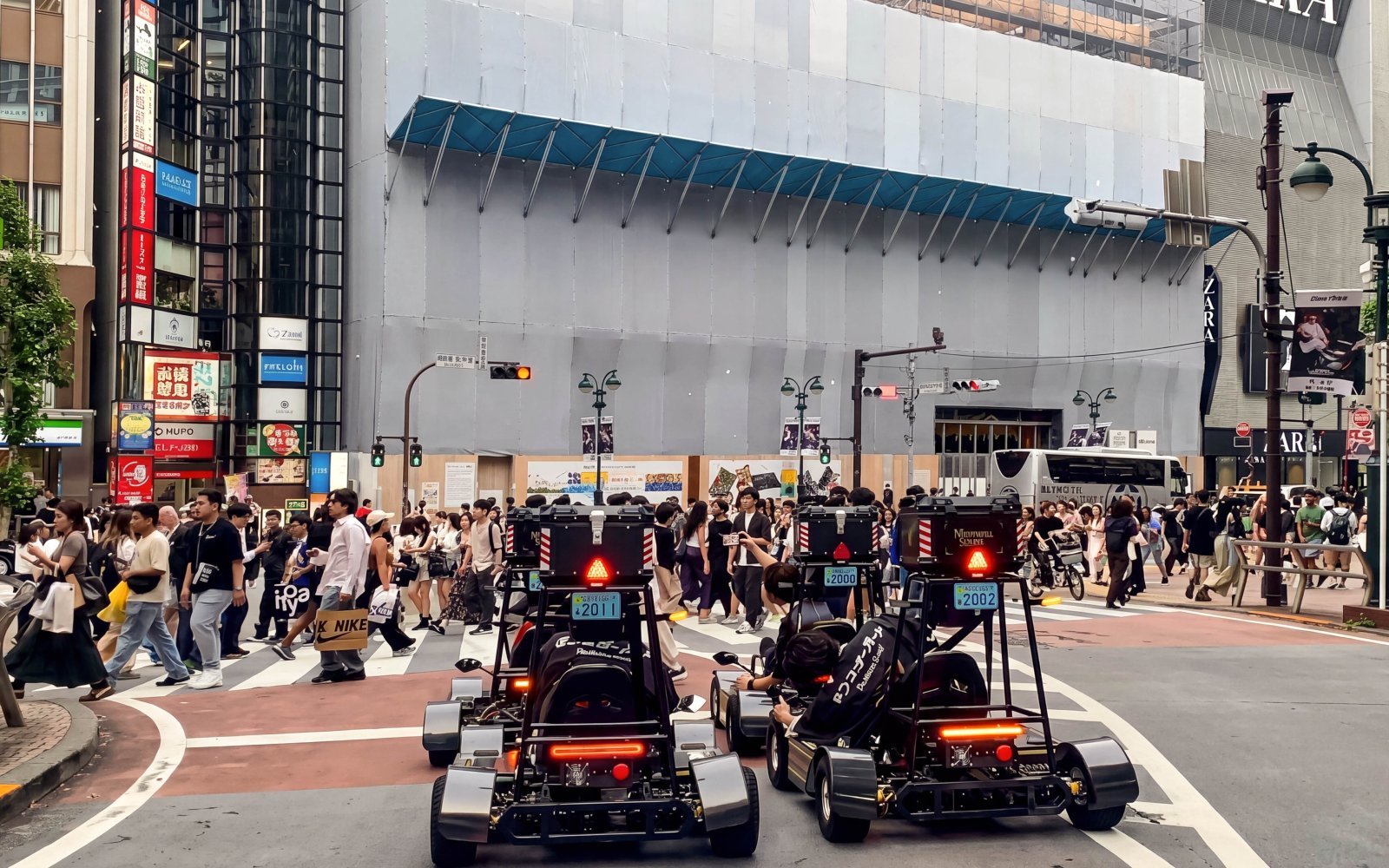 Go-karts driving through a busy intersection in Tokyo during a street kart experience.