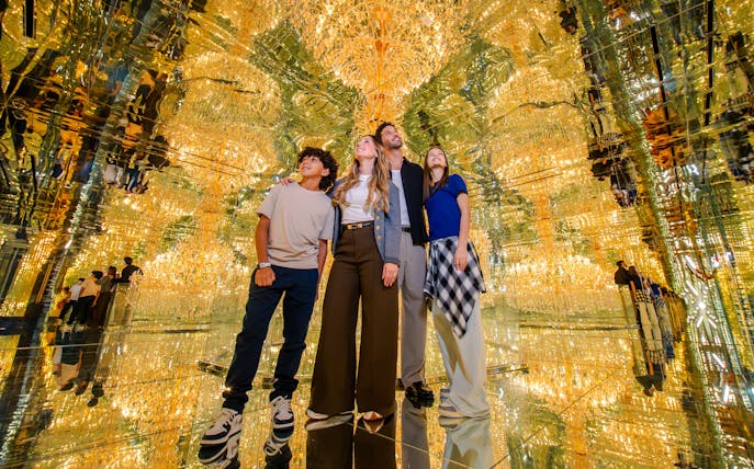Visitors exploring mirrored room at House of Hype, surrounded by golden reflections.
