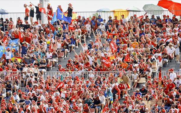 Fans cheering at Barcelona Formula 1 grandstand with flags and team colors.