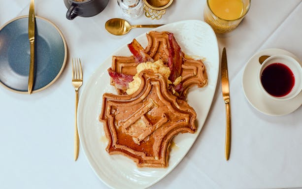 Waffles shaped like Hogwarts crest with bacon and eggs on a white plate.