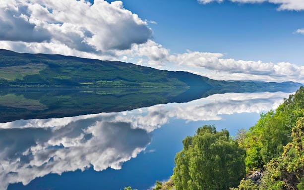 Scottish Highlands landscape with a calm lake reflecting clouds and green hills.