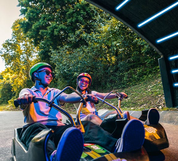 Friends riding luge carts into a tunnel on the Skyline Luge, Singapore.