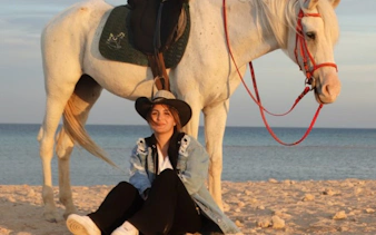 Person sitting on sandy beach with horse at Nabq Bay.