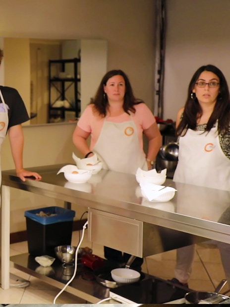 Small group in a Florence kitchen during a cooking class, wearing aprons and listening attentively.