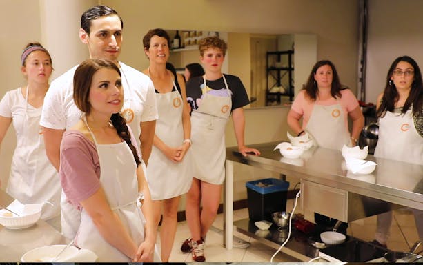 Small group in a Florence kitchen during a cooking class, wearing aprons and listening attentively.