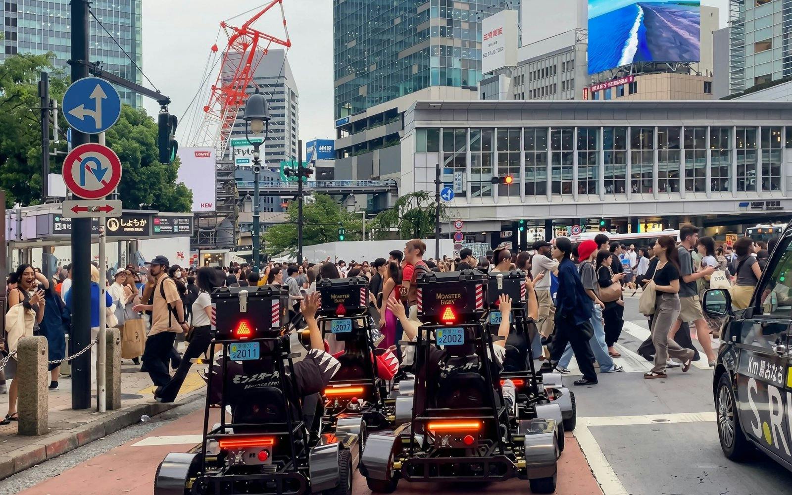 Street karts driving through a busy intersection in Tokyo with skyscrapers in the background.