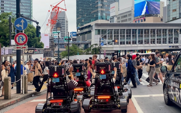 Street karts driving through a busy intersection in Tokyo with skyscrapers in the background.