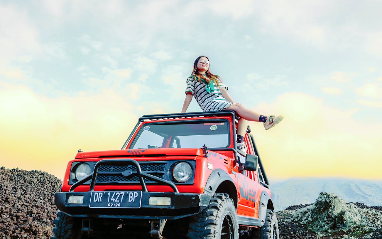 Person sitting on a red jeep during Mount Batur sunrise tour, Bali.