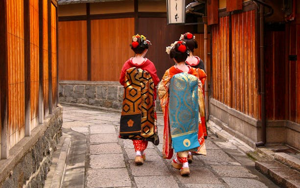 Geishas walking in traditional attire through Kyoto's historic district.