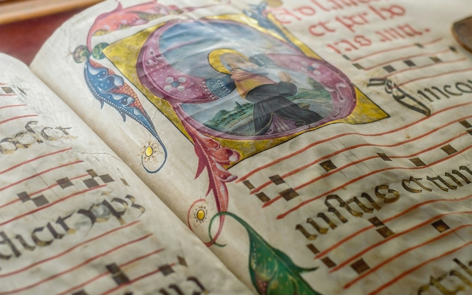 Illuminated choir book with ornate medieval illustrations and musical notations.