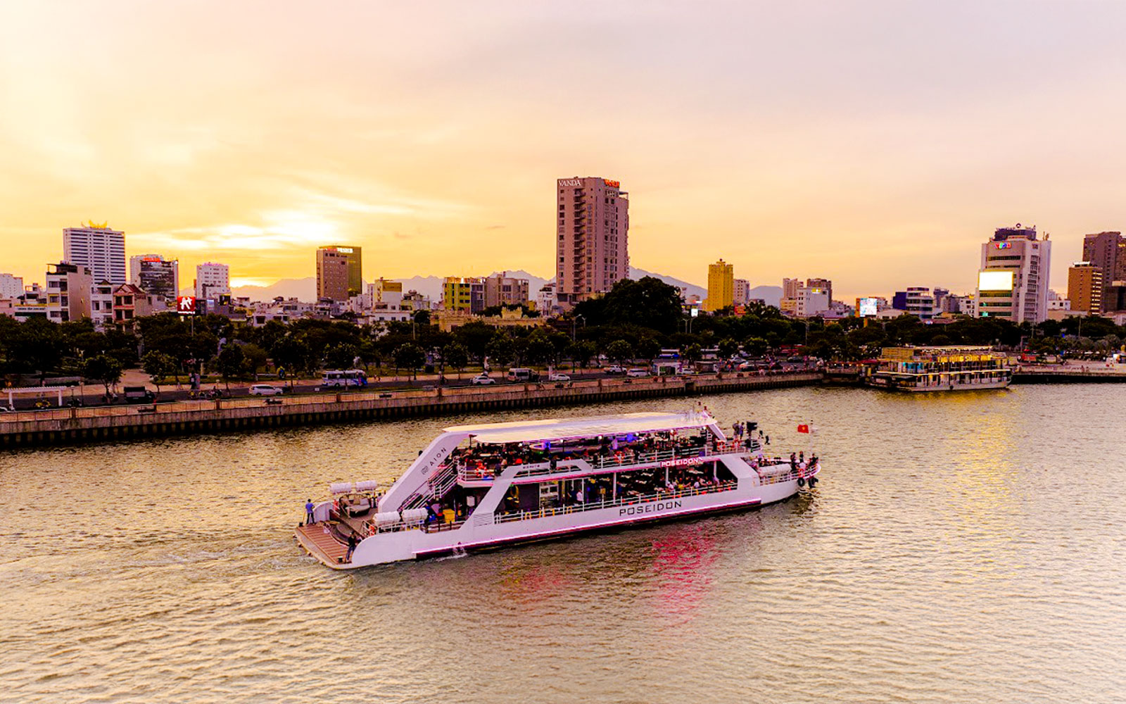 Da Nang Poseidon cruise on the river at sunset with city skyline in the background.