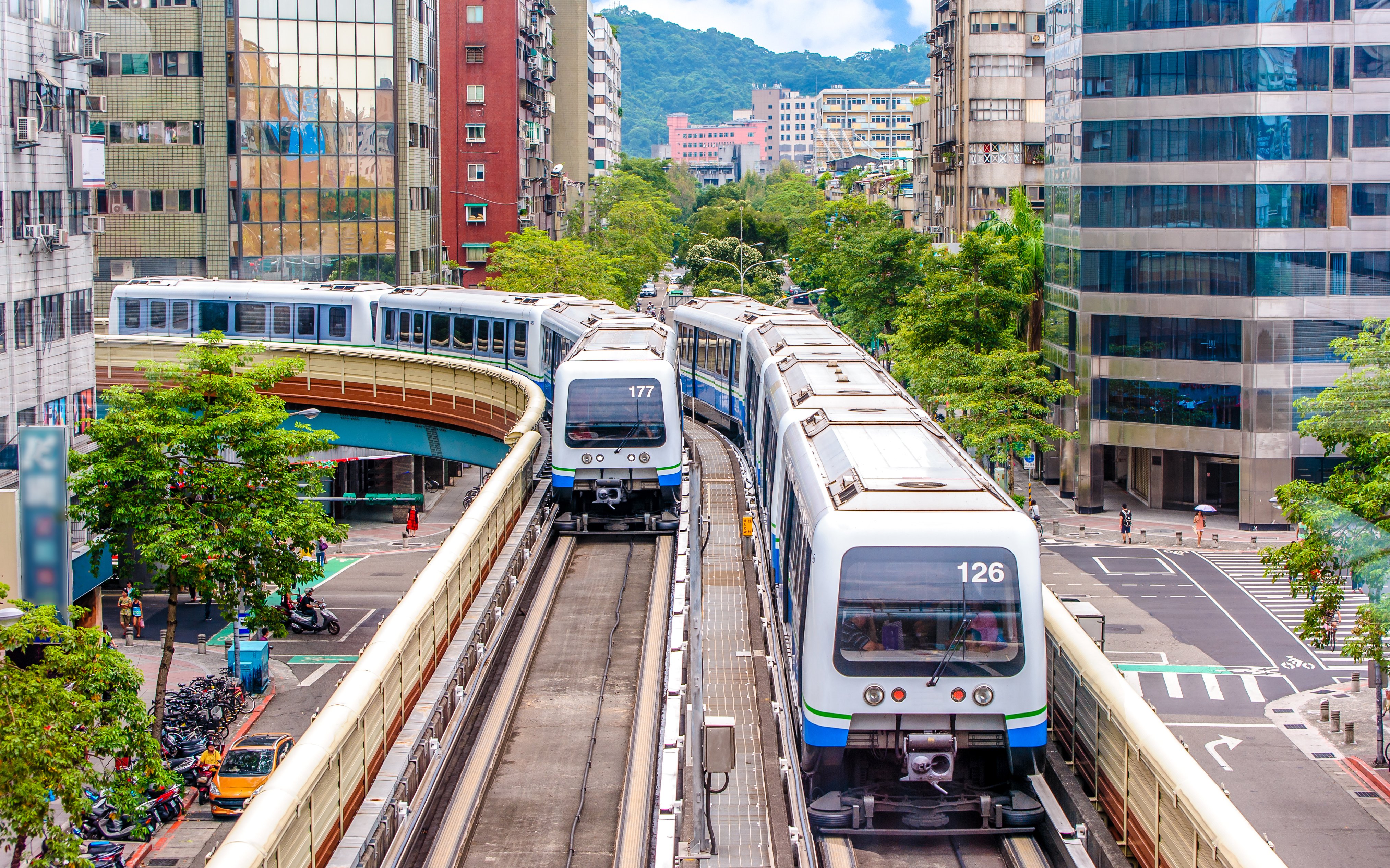 Taipei Metro trains on elevated tracks in urban cityscape.