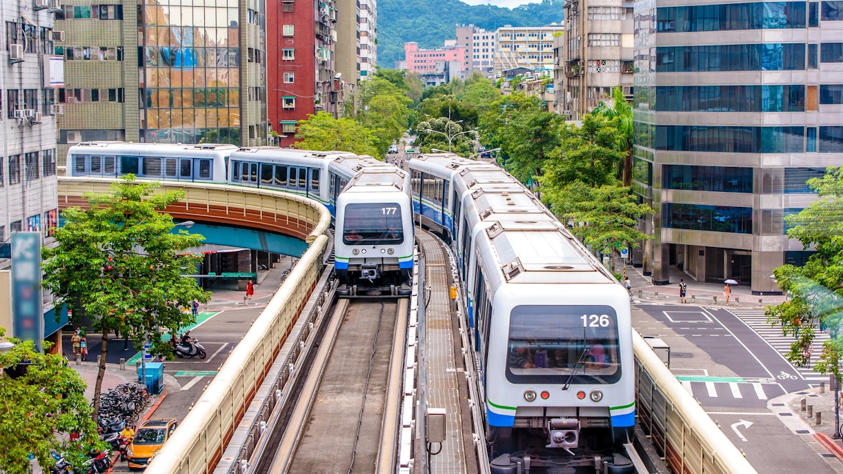 Taipei Metro trains on elevated tracks in urban cityscape.