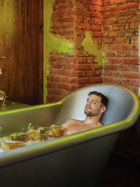 Couple relaxing in a beer spa bath with wooden and brick decor.