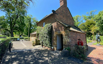 Historic cottage in Fitzroy Gardens, Melbourne, surrounded by lush greenery and a statue nearby.