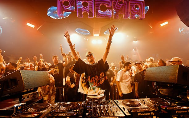 DJ performing at Pure Pacha Ibiza with crowd dancing under vibrant lights.