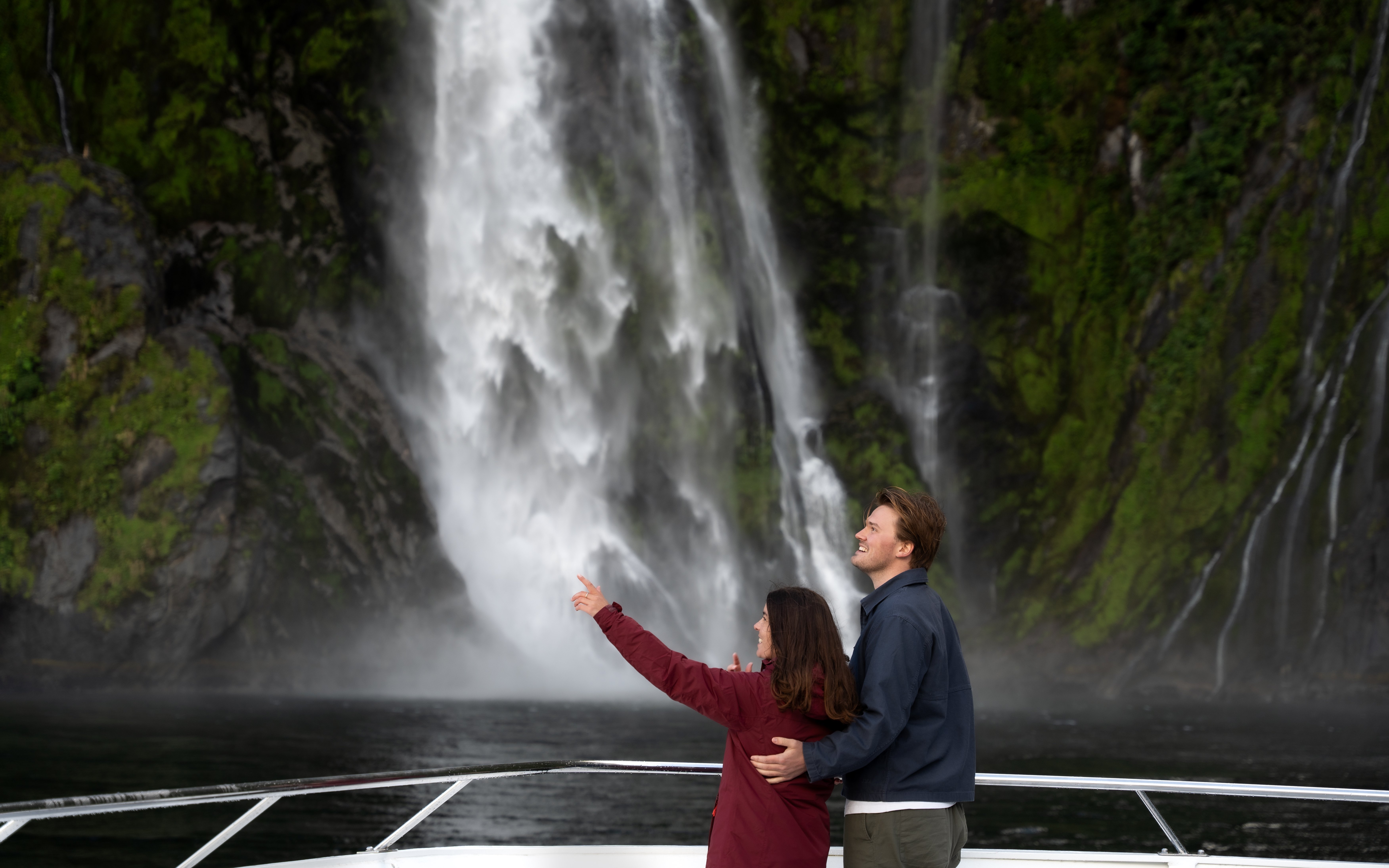 Couple enjoying waterfall view on Milford Sound cruise, New Zealand.