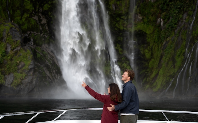 Couple enjoying waterfall view on Milford Sound cruise, New Zealand.