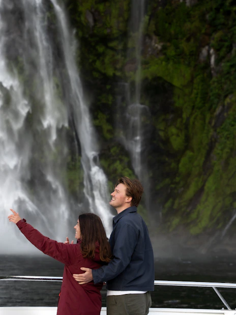 Couple enjoying waterfall view on Milford Sound cruise, New Zealand.