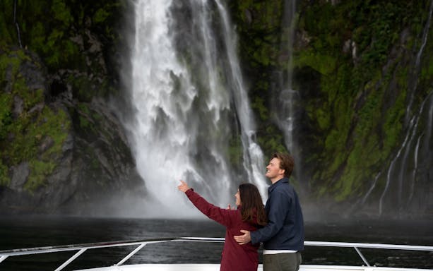 Couple enjoying waterfall view on Milford Sound cruise, New Zealand.