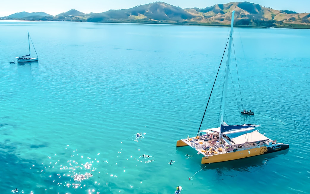 Catamaran sailing in clear waters near Fiji's South Sea with distant hills.