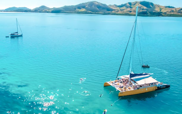 Catamaran sailing in clear waters near Fiji's South Sea with distant hills.