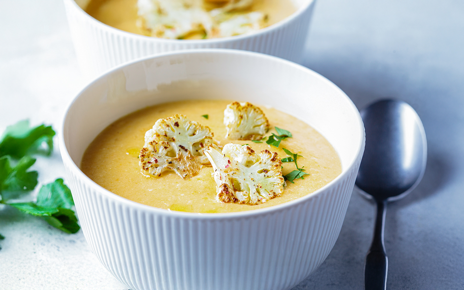 Vegetarian cream cheese soup with cauliflower served in a white bowl on a wooden table.