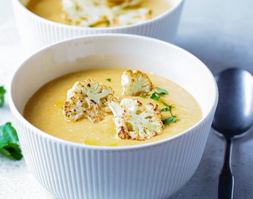 Vegetarian cream cheese soup with cauliflower served in a white bowl on a wooden table.