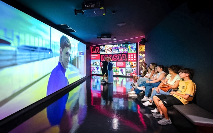 Visitors watching a video at La Masia exhibit in Spotify Camp Nou Barça Museum.