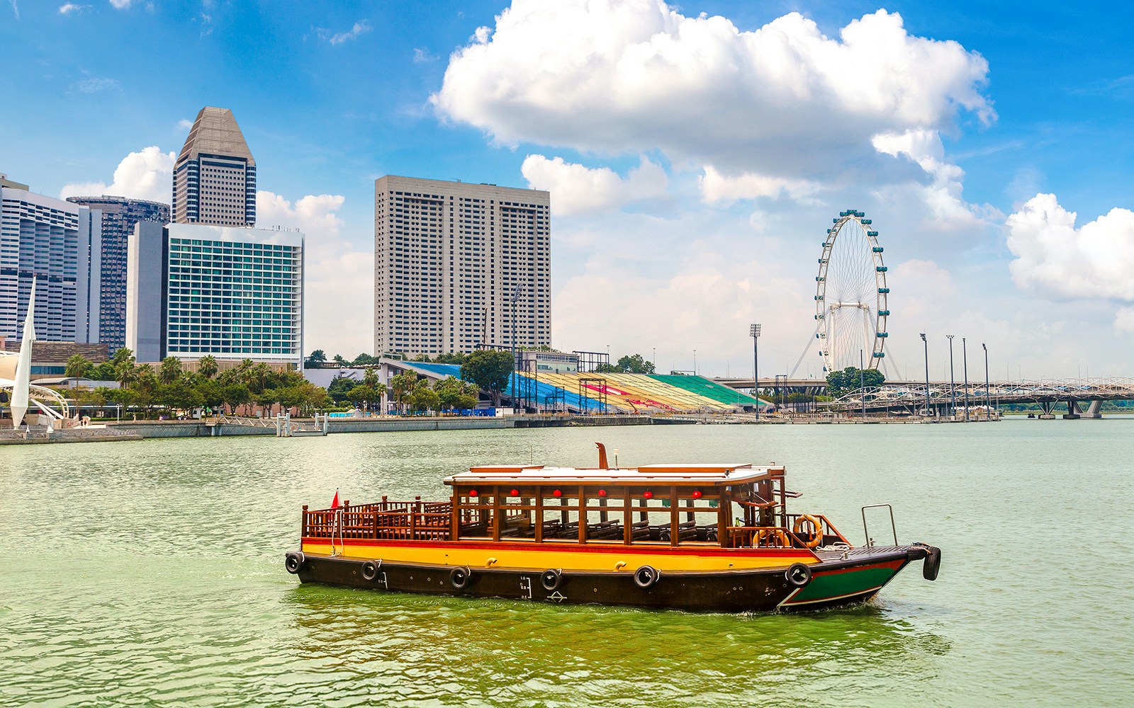 Boat on Singapore River with city skyline and Singapore Flyer in the background.