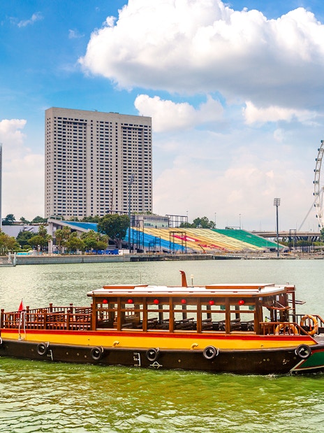 Boat on Singapore River with city skyline and Singapore Flyer in the background.