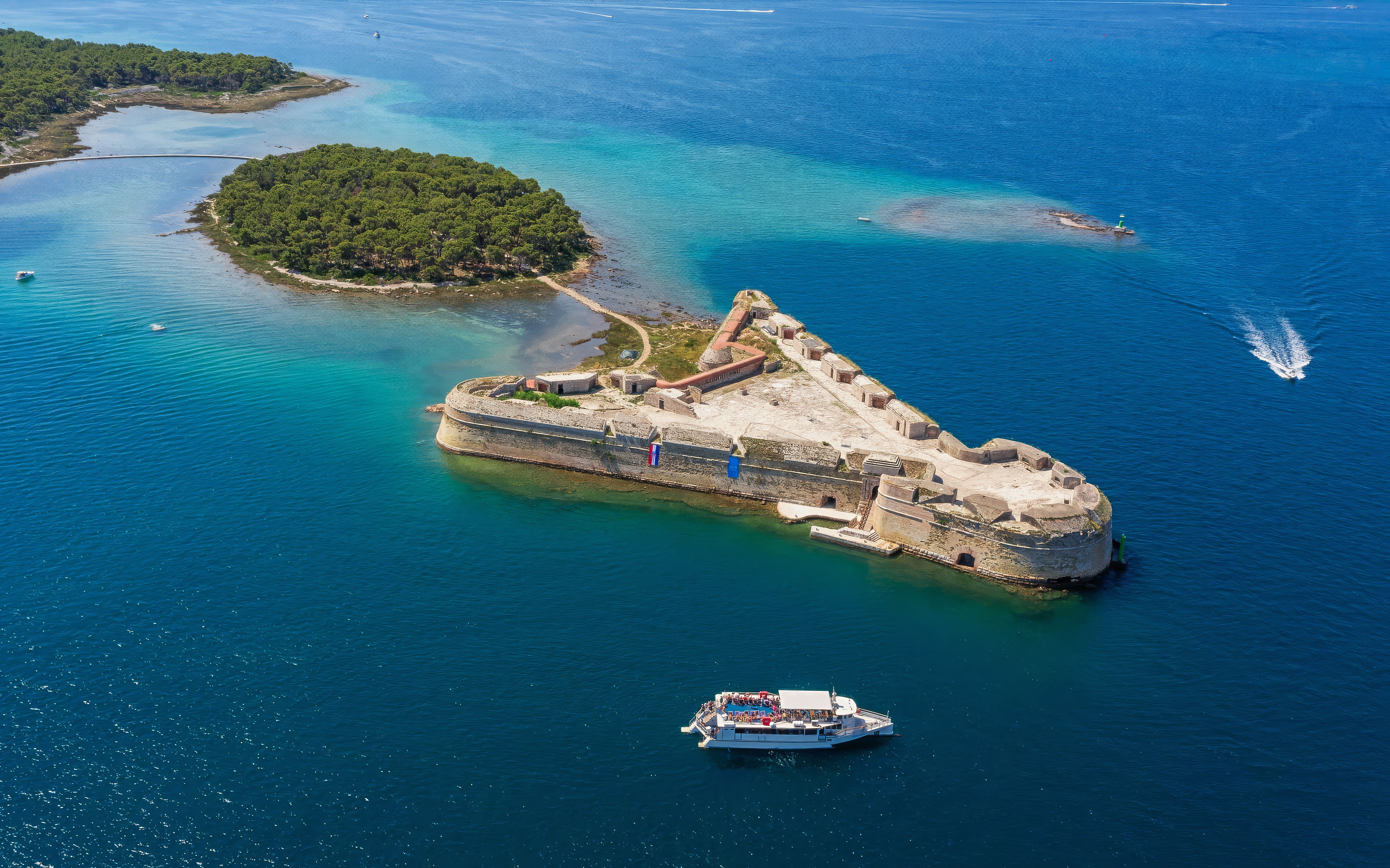 St Nicholas Fortress in Croatia surrounded by blue sea with a tour boat nearby.