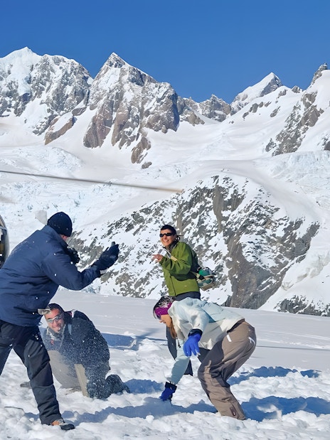People enjoying snow activities near a helicopter on Franz Josef Glacier, New Zealand.