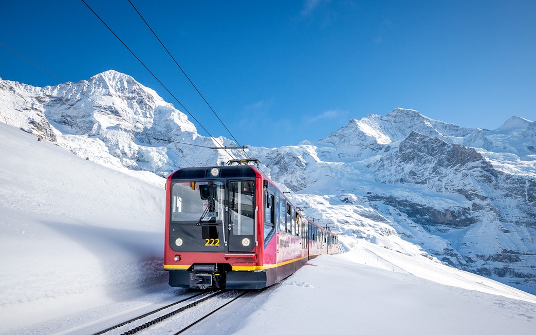 Red train traveling through snowy mountains on route from Grindelwald to Jungfraujoch.
