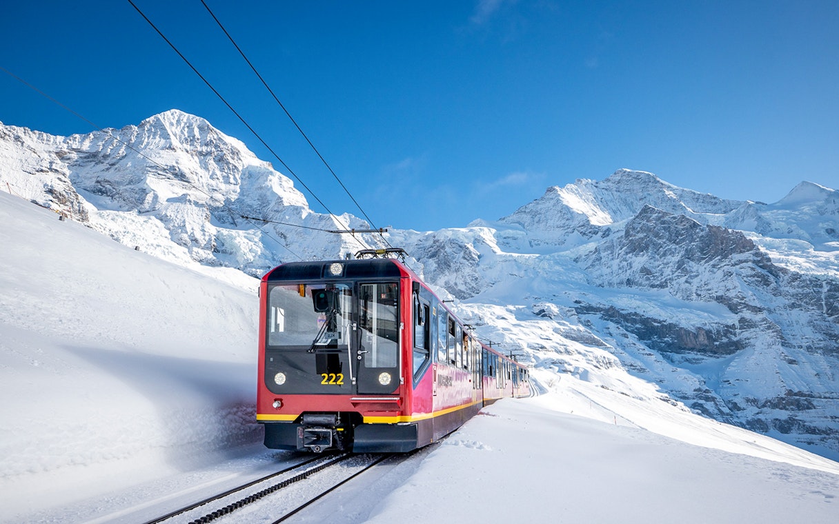 Red train traveling through snowy mountains on route from Grindelwald to Jungfraujoch.