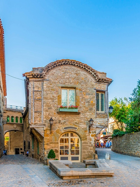 Historic stone building in Cité de Carcassonne, France, with ivy-covered walls and cobblestone street.