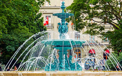 Fountain in Geneva with Swiss flags and historic building in the background.