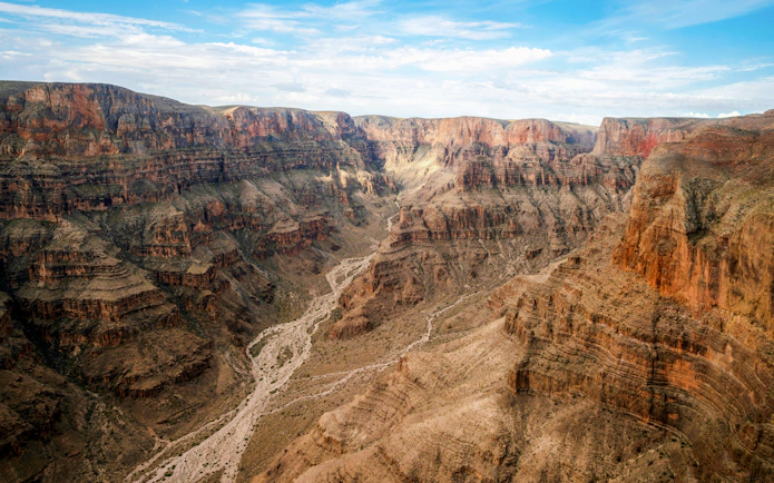 West Rim of the Grand Canyon with layered rock formations and a winding river below.