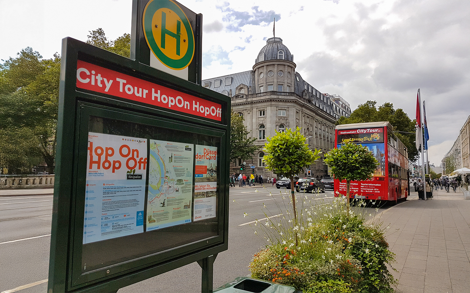 Hop-on hop-off bus stop with tour map and red double-decker bus in Düsseldorf.