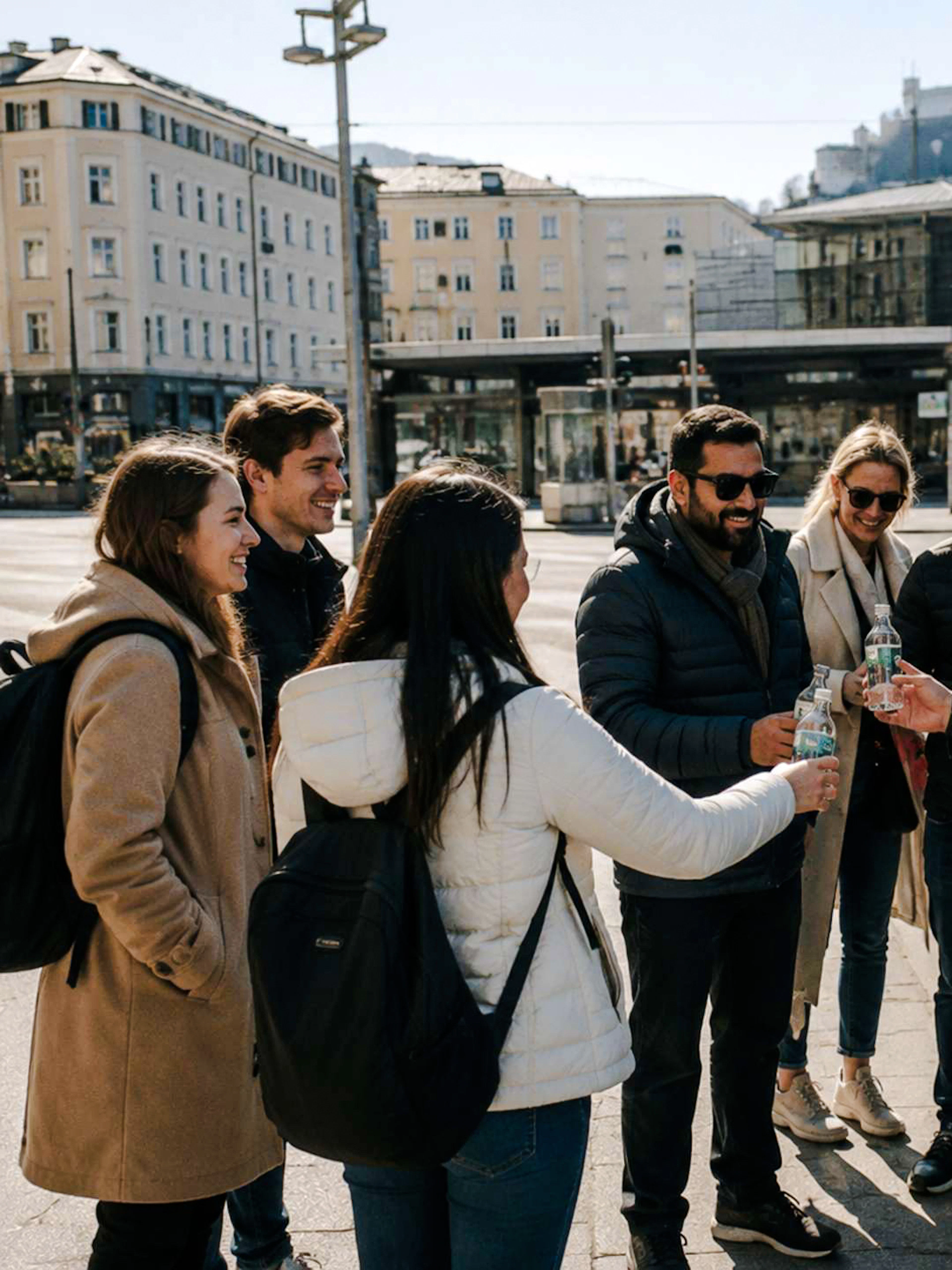 Group of tourists enjoying drinks near a van in Salzburg with Hohensalzburg Fortress in the background.