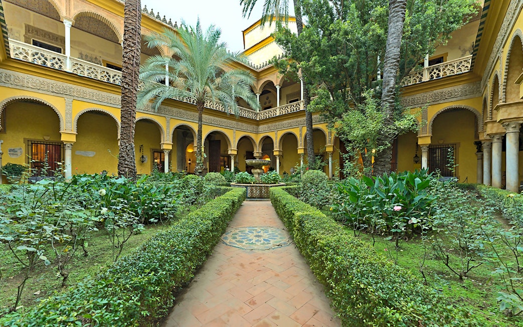 Palacio de las Dueñas courtyard with lush garden and central fountain in Seville.