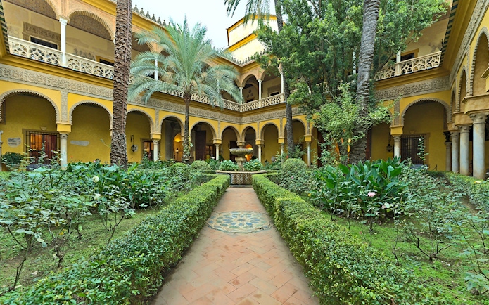 Palacio de las Dueñas courtyard with lush garden and central fountain in Seville.