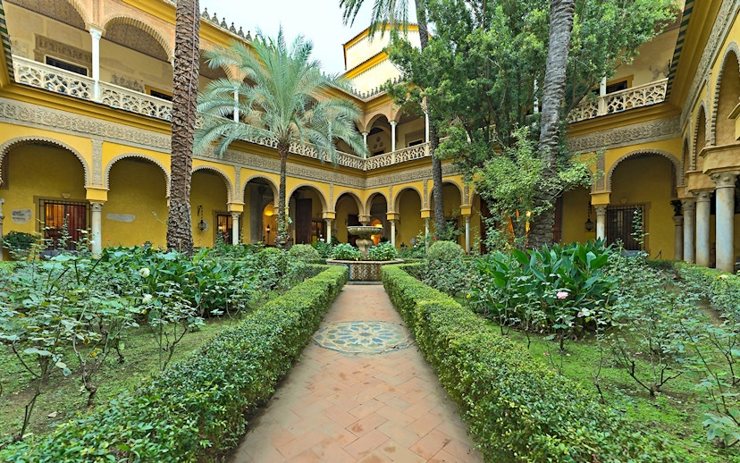 Palacio de las Dueñas courtyard with lush garden and central fountain in Seville.